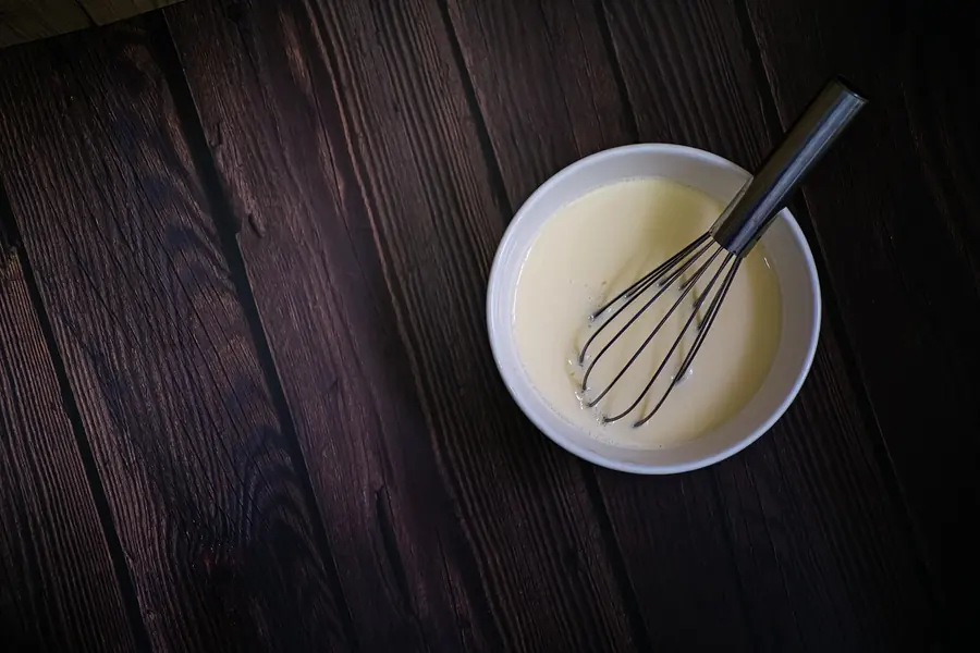 Bowl of smooth pancake batter with a whisk on a dark wooden table