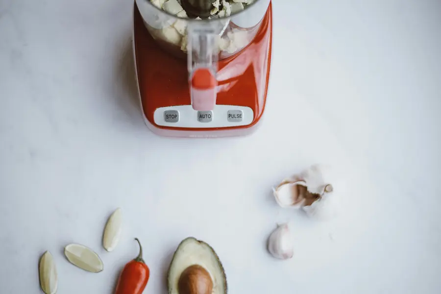 Red blender with garlic, a chili pepper and avocado on a white counter