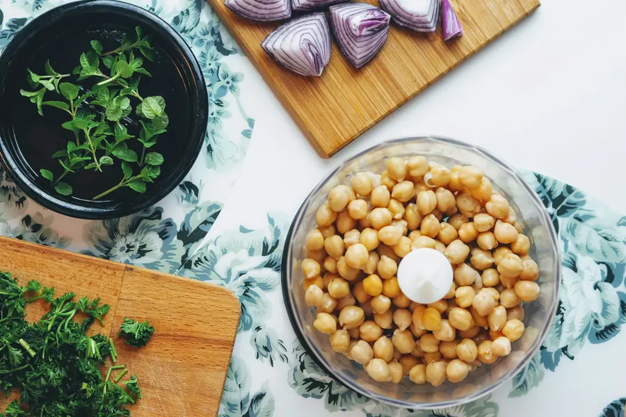 Chickpeas in a food processor bowl next to chopped herbs on a cutting board