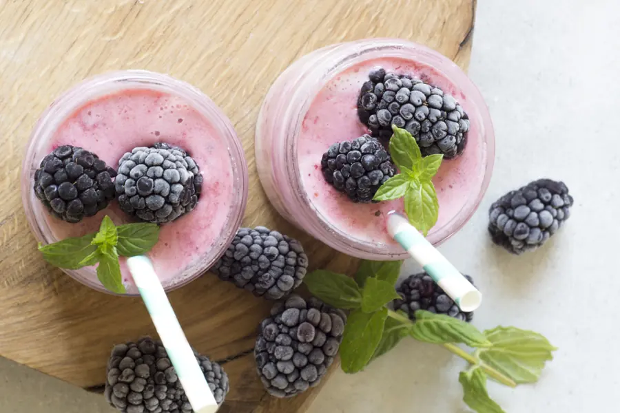 Two creamy blackberry smoothies with straws and fresh blackberries