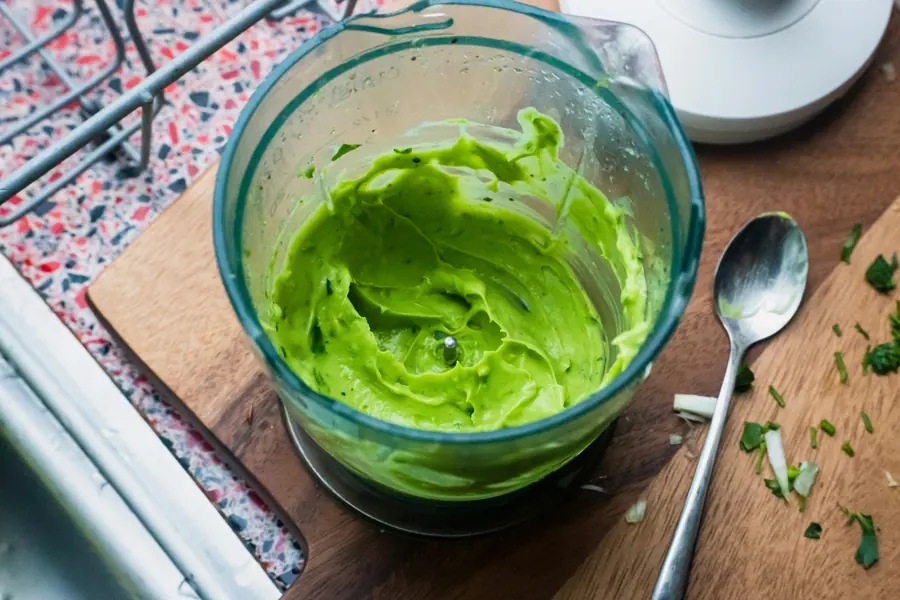 Smooth green purée in a blender container on a wooden board with a spoon