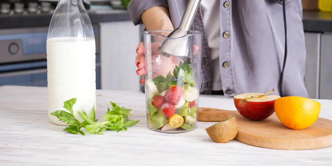 Person using an immersion blender in a tall cup in a grey home kitchen
