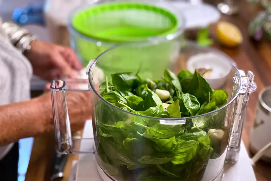 Clear processor bowl filled with fresh spinach leaves