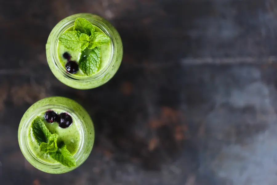 Two green smoothies with blueberries and mint on a dark surface