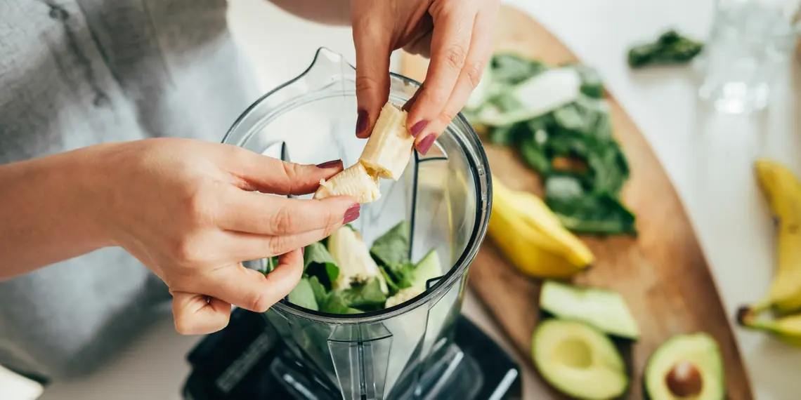 Hands adding sliced banana and avocado to a blender for a morning smoothie