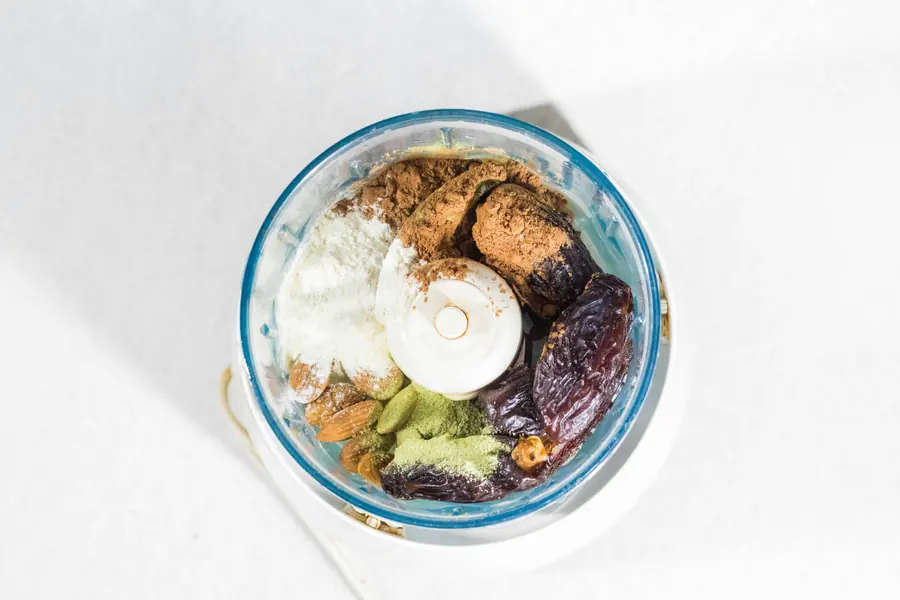 Overhead view of nuts, dates and cocoa in a food processor bowl before blending