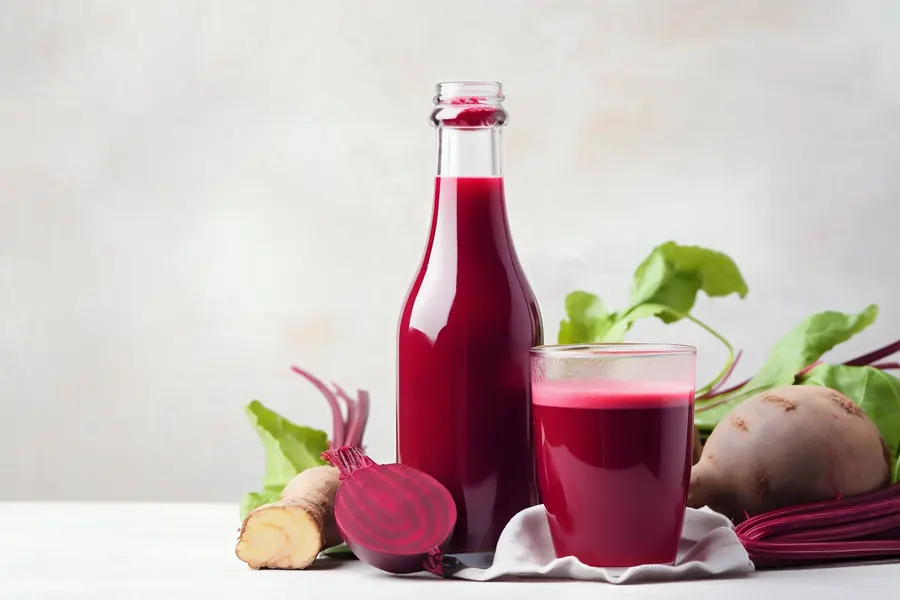 Bottle and glass of deep red beetroot juice beside fresh beets
