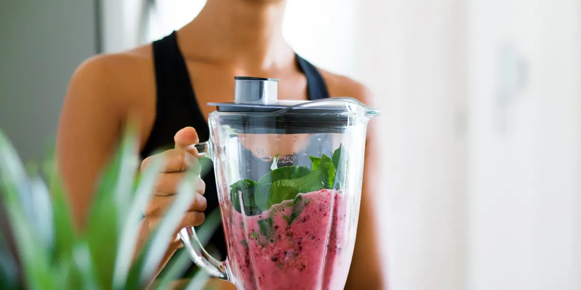 Woman holding a blender jar of deep pink berry smoothie with spinach