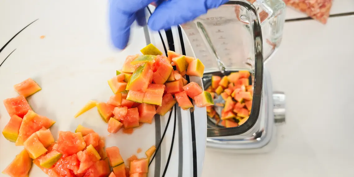 Chopped papaya and mango being added to a blender for a banana-free smoothie